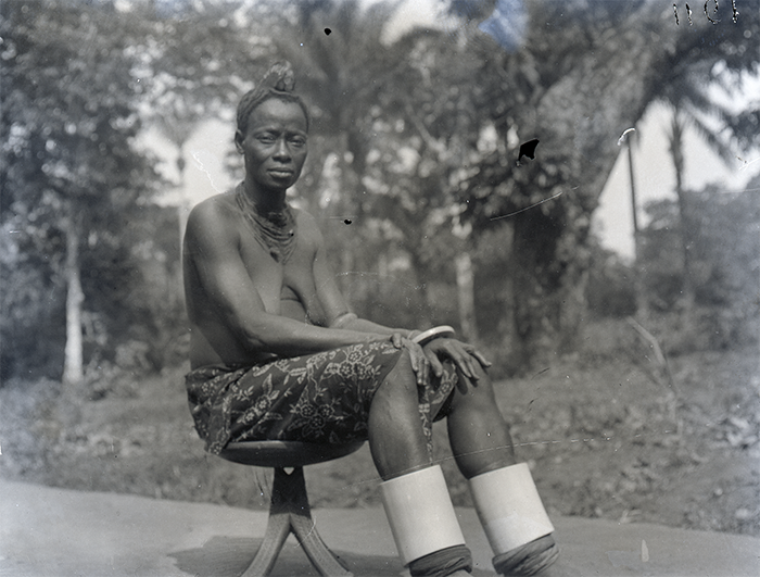 An Igbo elder from Awka with wooden head dress, set with pearl buttons, c. 1910-11